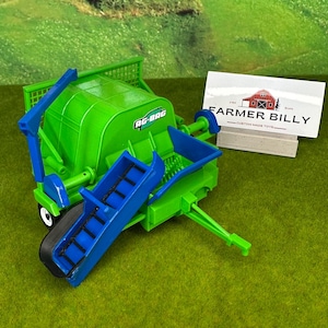 May include: Green and blue toy farm equipment with the words "AG-BAG" printed on the side. The toy is on a green grass surface with a business card that reads "FARMER BILLY CUSTOM MADE TOYS".