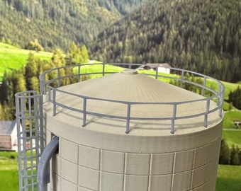 Könnte beinhalten: Ein weißer, zylindrischer Wasserturm mit einem quadratischen Gittermuster und einem Geländer oben. Der Turm steht vor dem Hintergrund grüner Hügel und einer Bergkette.