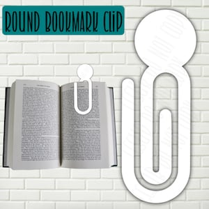 May include: White round bookmark clip with a large round top and a smaller round bottom. The clip is shaped like a paperclip and is designed to hold a page in a book.
