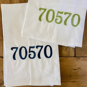 May include: Two white kitchen towels with the number 70570 embroidered on them. The top towel has the number in green thread, and the bottom towel has the number in dark blue thread.