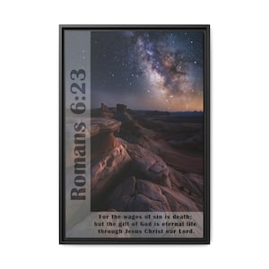 May include: A framed print with a black frame and a nighttime landscape image of a rocky desert with the Milky Way galaxy in the sky. The text "Romans 6:23" is on the left side of the image and the text "For the wages of sin is death; but the gift of God is eternal life through Jesus Christ our Lord." is at the bottom of the image.