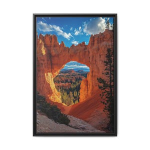 May include: A natural stone archway in a red rock canyon with a view of a forest and distant mountains through the opening. The sky is blue with white clouds.