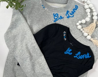 Puede incluir: Dos sudaderas, una gris y otra negra, con la frase "Le Luna" bordada en hilo azul en el cuello.