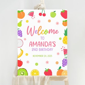 May include: A white sign decorated with vibrant fruit illustrations and the text "Welcome to Amanda's 2nd Birthday November 24, 2025". The design includes images of various fruits like strawberries and grapes.