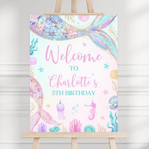 May include: Welcome to Charlotte's 5th Birthday mermaid themed party sign featuring a purple, pink, and blue mermaid tail with seashells and starfish.
