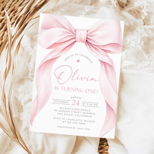 May include: A rectangular invitation card featuring a large, soft pink watercolor bow at the top. The text reads: Join us to celebrate Olivia is turning one! Saturday August 24 at 3:00 PM, Wilson's Residence, 55 Garden Street, San Diego, California.