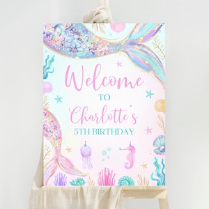 以下が含まれることがあります： 「Welcome to Charlotte's 5th Birthday」と書かれたピンクとブルーのマーメイドをテーマにしたウェルカムサイン。サインには、虹色の鱗、貝殻、ヒトデ、タツノオトシゴが付いたマーメイドの尻尾が描かれています。