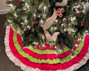 May include: A Christmas tree skirt with three layers of ruffles. The top layer is green, the middle layer is pink, and the bottom layer is white.
