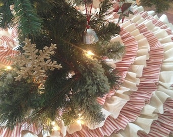 May include: A white and red striped Christmas tree skirt with multiple layers of ruffles. The skirt is made of fabric and has a vintage look.