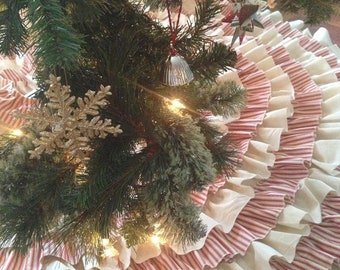 May include: A white and red striped Christmas tree skirt with multiple layers of ruffles. The skirt is made of fabric and has a vintage look.
