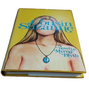 May include: A yellow book cover with a woman's face obscured by the title "Cousin Suzanne" in blue lettering. The text "A novel by Myrna Blyth" is printed in blue at the bottom of the cover.