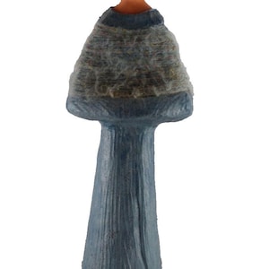 May include: A standing figurine of a person with a dark brown complexion and black hair. The figure wears a textured blue garment that flares out at the shoulders, featuring a light gray, fuzzy, wool-like material draped over the upper torso.