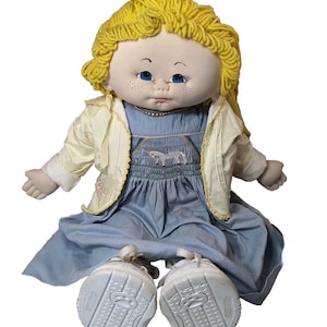 May include: A handmade cloth doll with blonde yarn hair, blue eyes, and a light blue dress. The doll is wearing a white jacket and white shoes.