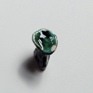 May include: A small, green ceramic vase with a unique, organic shape. The vase has a glossy finish and a slightly uneven surface.