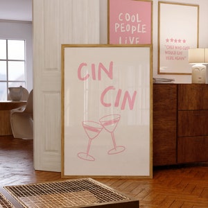 Puede incluir: Dos impresiones enmarcadas en rosa con el texto "Cool People Live" y "Cin Cin" con un gráfico de dos copas de martini brindando.