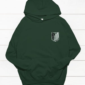 May include: A dark green hooded sweatshirt with a white graphic of the Attack on Titan logo on the front.