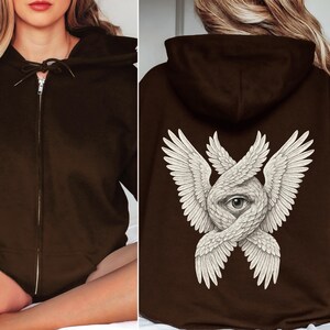 May include: A dark brown zip-up hoodie. The front features a drawstring hood and a full-length zipper. The back displays a detailed white illustration of an eye surrounded by intertwined wings. The hoodie is a casual garment.