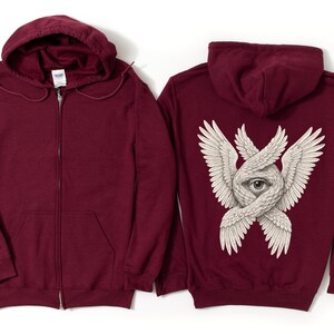 May include: A maroon zip-up hoodie with a hood and front pockets. The back of the hoodie features a detailed graphic of an eye surrounded by intertwined wings in white. The hoodie is made of a soft material.