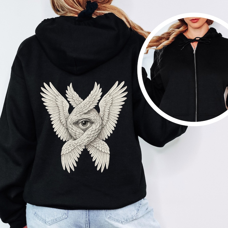 May include: Black zip-up hoodie featuring a detailed cream-colored illustration on the back. The design depicts a central eye surrounded by intertwined wings. The hoodie has a drawstring hood and a full-length zipper.