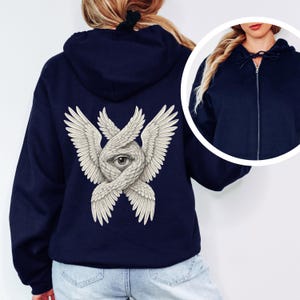 May include: Navy blue zip-up hoodie featuring a detailed graphic on the back. The graphic depicts an eye within intertwined wings, rendered in a detailed, off-white color. The hoodie has a drawstring hood and a full-length zipper.