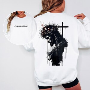 May include: White sweatshirt featuring a black and white graphic of Jesus wearing a crown of thorns and a cross. The front of the sweatshirt has the text "CHRIST IS KING" in black.