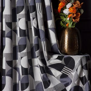 May include: Curtain fabric with a geometric pattern in grey, black, and white. The design includes semi-circles, squares, and stripes. A gold vase with orange and white flowers is also visible.