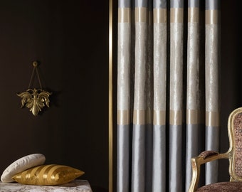 Pode incluir: Cortinas cinzas com guarnição dourada e um painel branco texturizado. As cortinas estão penduradas em um quarto com uma parede marrom e uma cadeira dourada.