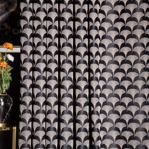 Könnte beinhalten: Schwarz-beige gemusterte Vorhänge. Die Vorhänge zeigen ein sich wiederholendes fächerförmiges Design in Beige auf schwarzem Hintergrund. Der Stoff ist in vertikalen Falten drapiert, wodurch ein strukturiertes Aussehen entsteht. Die Vorhänge werden wahrscheinlich für die Inneneinrichtung verwendet.