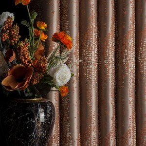 Op de afbeelding: Een decoratief arrangement met een zwarte marmeren vaas met gouden accenten, gevuld met oranje en witte bloemen. De achtergrond toont getextureerde, bruine gordijnen met een subtiel patroon.