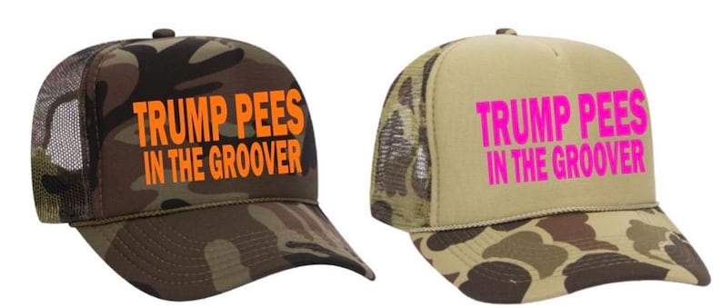 Pu&ograve; includere: Due cappellini da camionista con la scritta "TRUMP PEES IN THE GROOVER". Un cappellino ha un motivo mimetico con testo arancione, l'altro ha un motivo beige e mimetico con testo rosa.