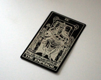 Puede incluir: Carta de tarot en blanco y negro con la imagen de un rey sentado en un trono. La carta está etiquetada como "THE EMPEROR." y "IV."