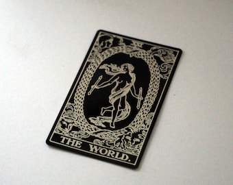 Puede incluir: Una carta de tarot negra con una ilustración blanca de una mujer de pie en un círculo con una serpiente. El texto "THE WORLD." está impreso en la parte inferior de la carta.