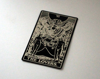 Puede incluir: Carta de tarot en blanco y negro con la imagen de dos figuras de pie a cada lado de un árbol. La carta se titula "THE LOVERS."
