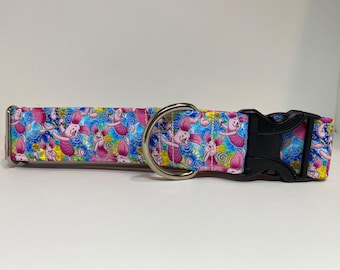 May include: A pink and blue dog collar with a colorful pattern of cartoon piglets. The collar has a silver D-ring and a black plastic buckle.