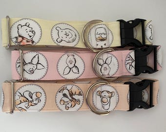 May include: Three dog collars with different Winnie the Pooh character designs. The top collar is yellow with a Winnie the Pooh design, the middle collar is pink with a Piglet design, and the bottom collar is peach with a Tigger design.