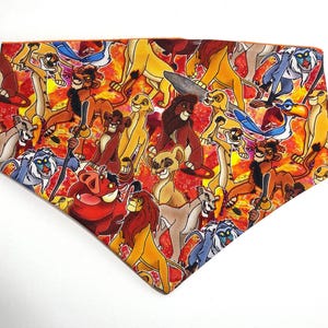 May include: A colorful bandana featuring a repeating pattern of characters from the Lion King movie. The bandana is orange with a red, yellow, and blue pattern. The characters include Simba, Mufasa, Scar, Nala, Timon, Pumbaa, and Zazu.