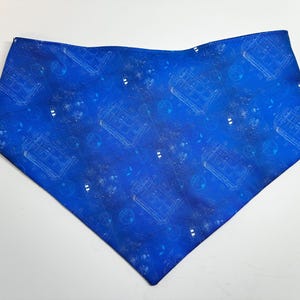 May include: Blue bandana with a repeating white pattern of a police box, circles, and other shapes. The bandana is a square shape folded in half to create a triangle.