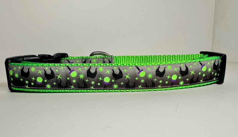 Op de afbeelding: Een groene hondenriem met een zilveren en zwart lint met een herhalend patroon van een heksenhoed en een groene bol.