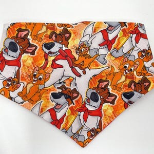 May include: A colorful bandana with a repeating pattern of cartoon dogs and cats. The bandana is orange, white, and brown with a red bandana on each dog.