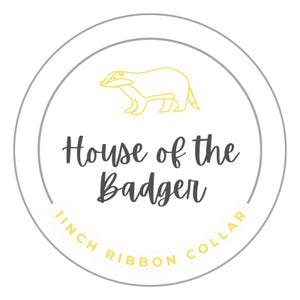 May include: A gray circle with a yellow outline and a yellow badger illustration inside. The text "House of the Badger" is in black text inside the circle. The text "1 inch Ribbon Collar" is in yellow text around the outside of the circle.