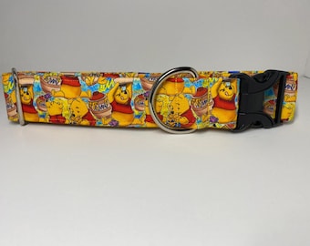 May include: A yellow dog collar with a Winnie the Pooh print. The collar has a silver D-ring and a black plastic buckle.