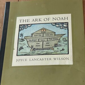 Peut inclure: Une couverture de livre verte avec le titre "L'Arche de Noé" et une illustration de l'Arche de Noé avec différents compartiments étiquetés "Nourriture humaine", "Nourriture animale", "Dormeurs de jour", "Insectes", "Dormeurs de nuit", "Animaux domestiques" et "Animaux sauvages". Le nom de l'auteur, "JOYCE LANCASTER WILSON", est imprimé sous l'illustration.