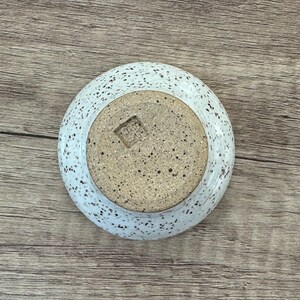 May include: White ceramic bowl with speckled brown glaze. The bowl has a small square indentation on the bottom.