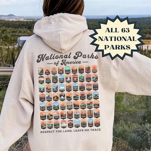 May include: A beige hoodie with a graphic of all 63 National Parks of America on the back. The graphic includes the park names and logos. The text "Respect the Land, Leave No Trace" is printed below the graphic. The hoodie has a drawstring hood and a kangaroo pocket. The text "ALL 63 NATIONAL PARKS" is printed on a starburst sticker on the right side of the image. The text "RED PRAIRIE GOODS & GIFTS EST 2024" is printed on a sticker on the bottom right of the image.
