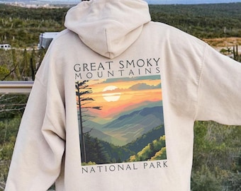 May include: A cream-colored hoodie with a graphic print of a sunset over the Great Smoky Mountains National Park. The text "Great Smoky Mountains National Park" is printed below the image.
