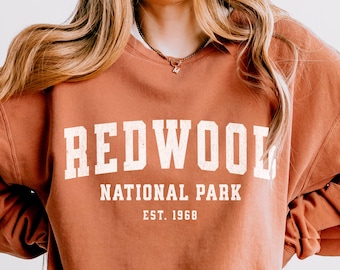 May include: A rust-colored sweatshirt with the text "REDWOOD NATIONAL PARK EST. 1968" in white.