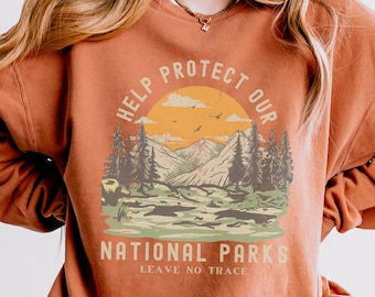 以下が含まれることがあります： 山と木々、そして「Help Protect Our National Parks Leave No Trace」というテキストが描かれた、ヴィンテージスタイルのグラフィックデザインが施された、さび色のスウェットシャツです。