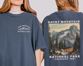 May include: A navy blue oversized t-shirt with a graphic print of the Rocky Mountain National Park logo on the front and a scenic image of the park on the back. The text on the back reads "Rocky Mountain National Park, Colorado, USA."