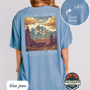 May include: Blue jean colored t-shirt featuring a graphic of Grand Teton National Park. The design includes a mountain range, trees, and the text "GRAND TETON NATIONAL PARK WYOMING EST. 1929". A smaller design is on the front.