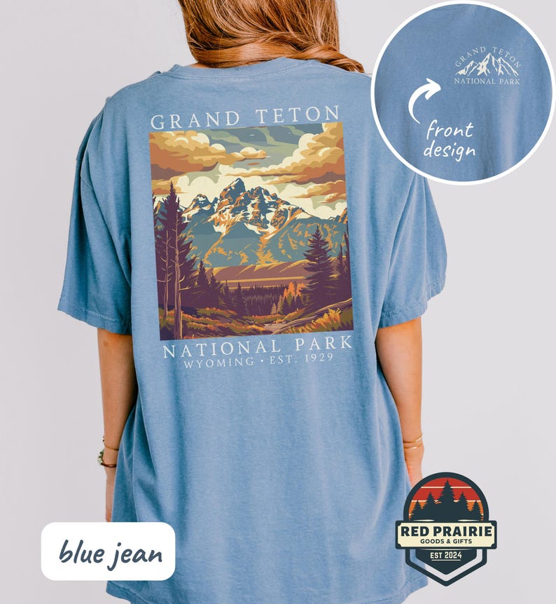 May include: Blue jean colored t-shirt featuring a graphic of Grand Teton National Park. The design includes a mountain range, trees, and the text "GRAND TETON NATIONAL PARK WYOMING EST. 1929". A smaller design is on the front.